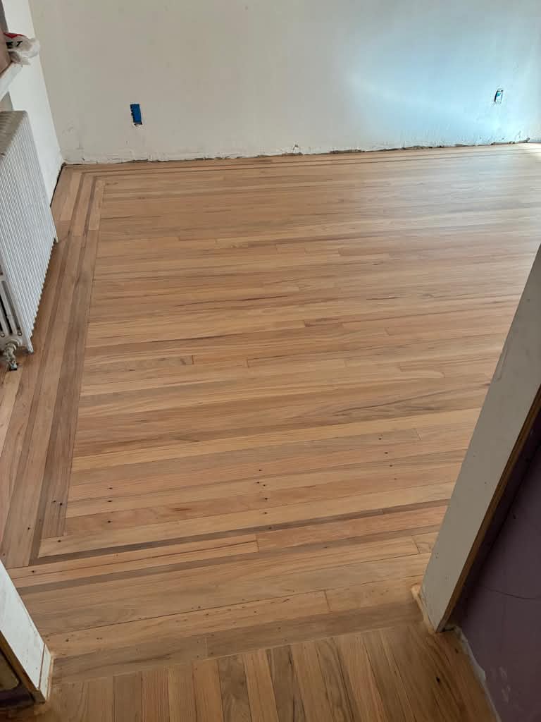 New light red oak with a darker border in a Flatbush room, walls unfinished